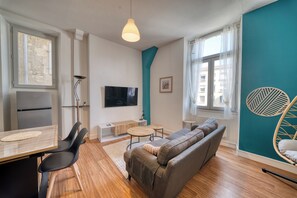 A modern living room with a sofa, a dining table, a TV, and a kitchen area with a fridge.