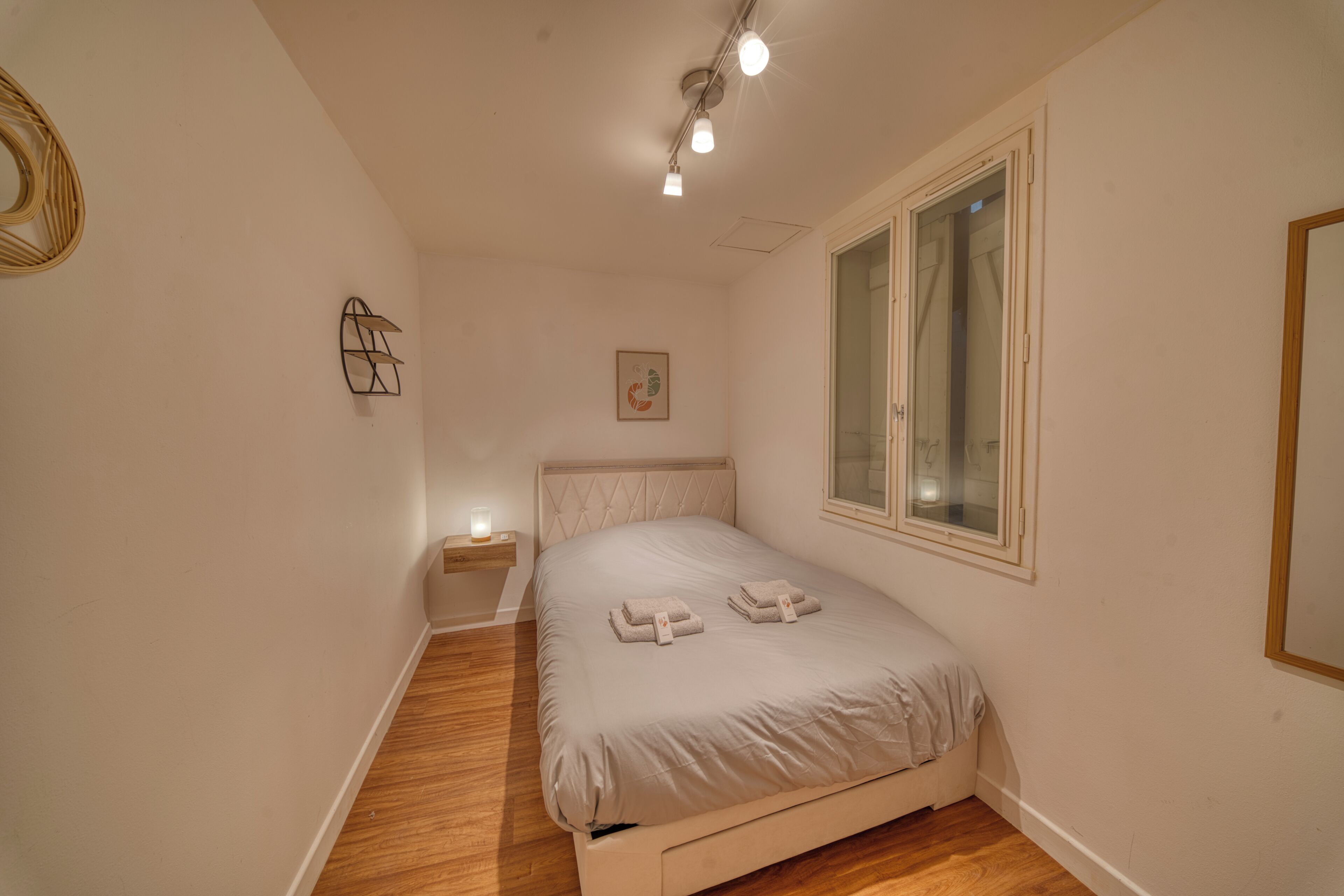 Een slaapkamer met een bed, nachtkastje, raam en wandlamp.