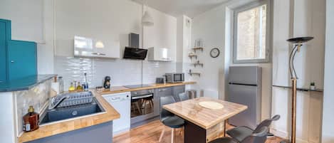 A compact kitchen with a dishwasher, microwave, and a refrigerator. There is a dining table with chairs and a small window providing natural light.