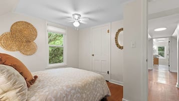 Quarto com cama, ventoinha no teto, janela e porta.