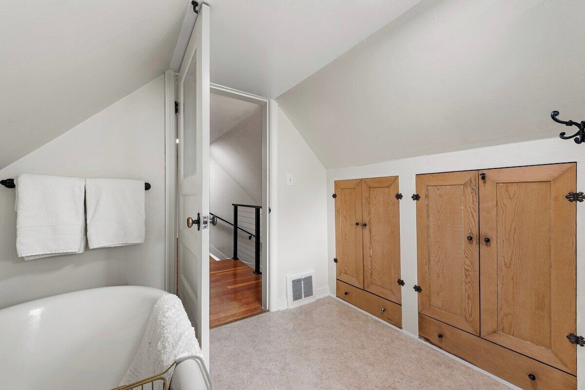 Un dormitorio con una bañera blanca, armarios de madera y una escalera que conduce a otra habitación.
