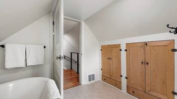 Un dormitorio con una bañera blanca, armarios de madera y una escalera que conduce a otra habitación.