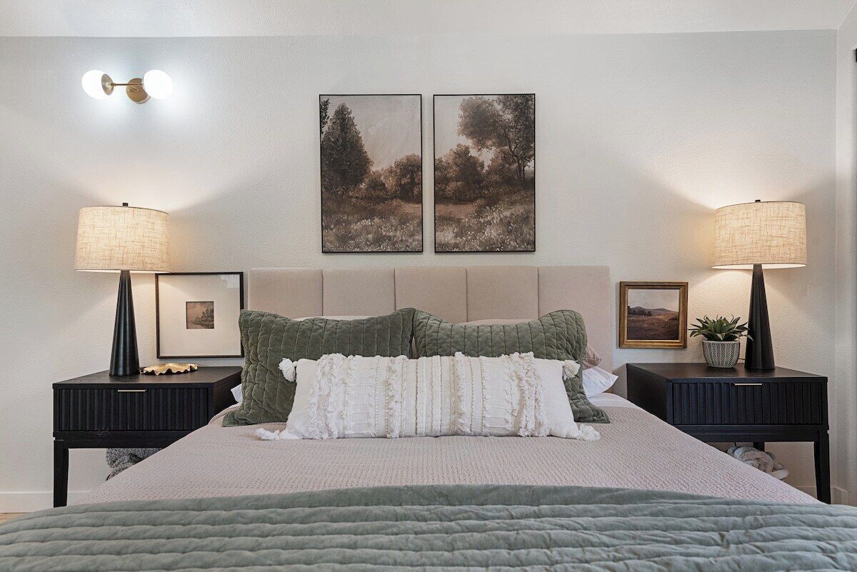 A bedroom with a bed, two nightstands, two wall-mounted lamps, and two framed pictures.
