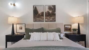 A bedroom with a bed, two nightstands, two wall-mounted lamps, and two framed pictures.