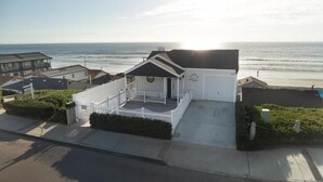 A coastal property with a white building featuring a porch, a garage, and a view of the ocean. - Fabulous 2 bed Home in Oceanside, beachfront access with stunning sea views (Oceanside)