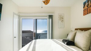 A hotel room with a bed, a view through a sliding door to the outside, and a painting on the wall. - Fabulous 2 bed Home in Oceanside, beachfront access with stunning sea views (Oceanside)