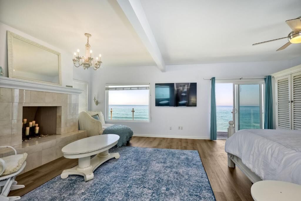 A bedroom with a bed, a fireplace, a table, and a view of the sea.