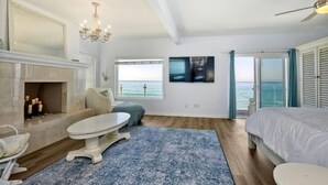 A bedroom with a bed, a fireplace, a table, and a view of the sea. - Fabulous 4 Bed Home Oceanfront Getaway in Oceanside, Fire Pit, Private Beach (Oceanside)