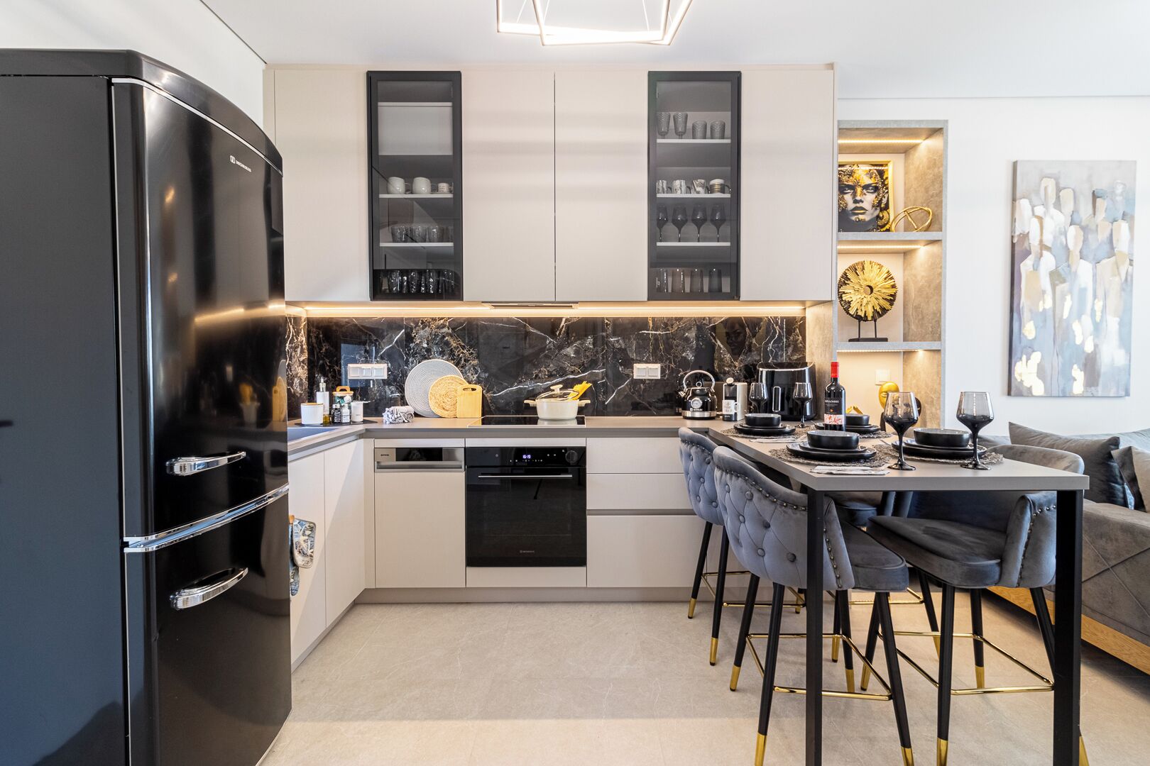 Una cocina moderna con un refrigerador negro, armarios empotrados, una isla central con asientos y un área de comedor con mesa y sillas.