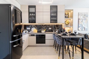 Una cocina moderna con un refrigerador negro, armarios empotrados, una isla central con asientos y un área de comedor con mesa y sillas.