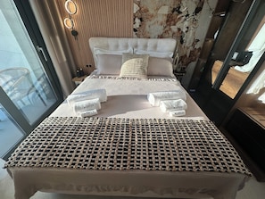 Ein Bett mit einer karrierten Kopfteile, mehreren Kissen und ordentlich gefalteten Handtüchern mit einem Markennamen.