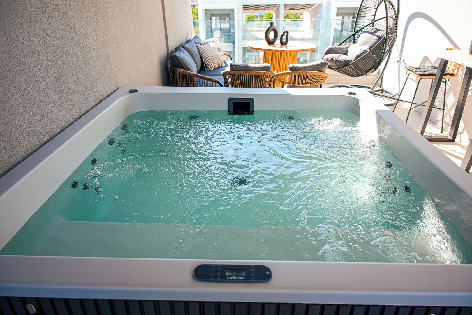 Ein Whirlpool mit Bedienfeld, umgeben von Korbmöbeln und einem Glastisch.