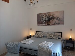 A bedroom with a bed, two nightstands, a chandelier, a painting, and two patterned chairs. - Adorable 2-bedroom apartment with AC in the center of charming Noto (Noto)