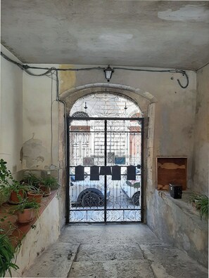 A narrow corridor with a metal gate leading to a street. There are potted plants on the left and a small shelf on the right. - Adorable 2-bedroom apartment with AC in the center of charming Noto (Noto)