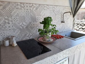 Una cucina con piastrelle decorate, una pianta in vaso, un lavandino e un tagliere.