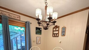Uma área de refeições com mesa redonda, quatro cadeiras, um lustre e vista através de uma porta de vidro.