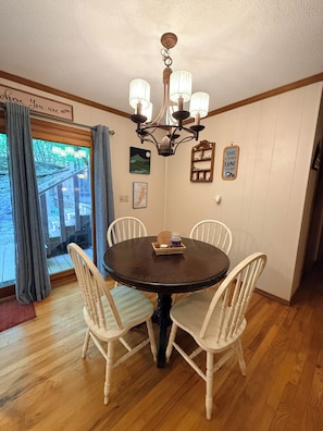 A dining area with a round table, four chairs, a chandelier, and a view through a glass door. - Howling Hideaway - Woodland Retreat, 2 king beds, Hot tub (Mentone)