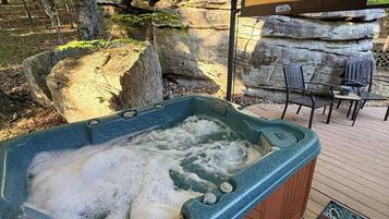 A hot tub under a canopy, surrounded by rocks and trees.
