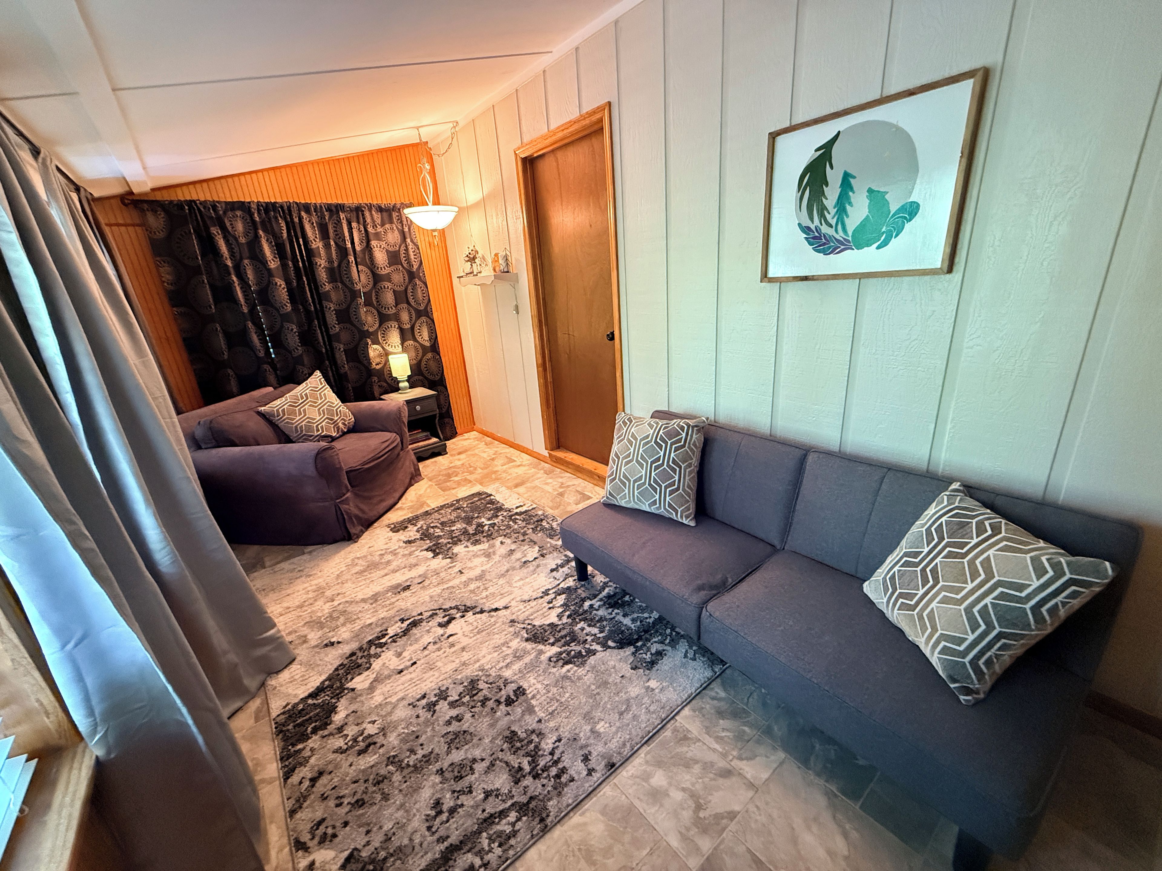 Ett vardagsrum med en soffa, en matta, en lampa och en dörr.