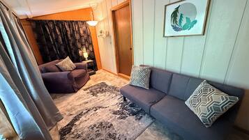 Ett vardagsrum med en soffa, en matta, en lampa och en dörr.