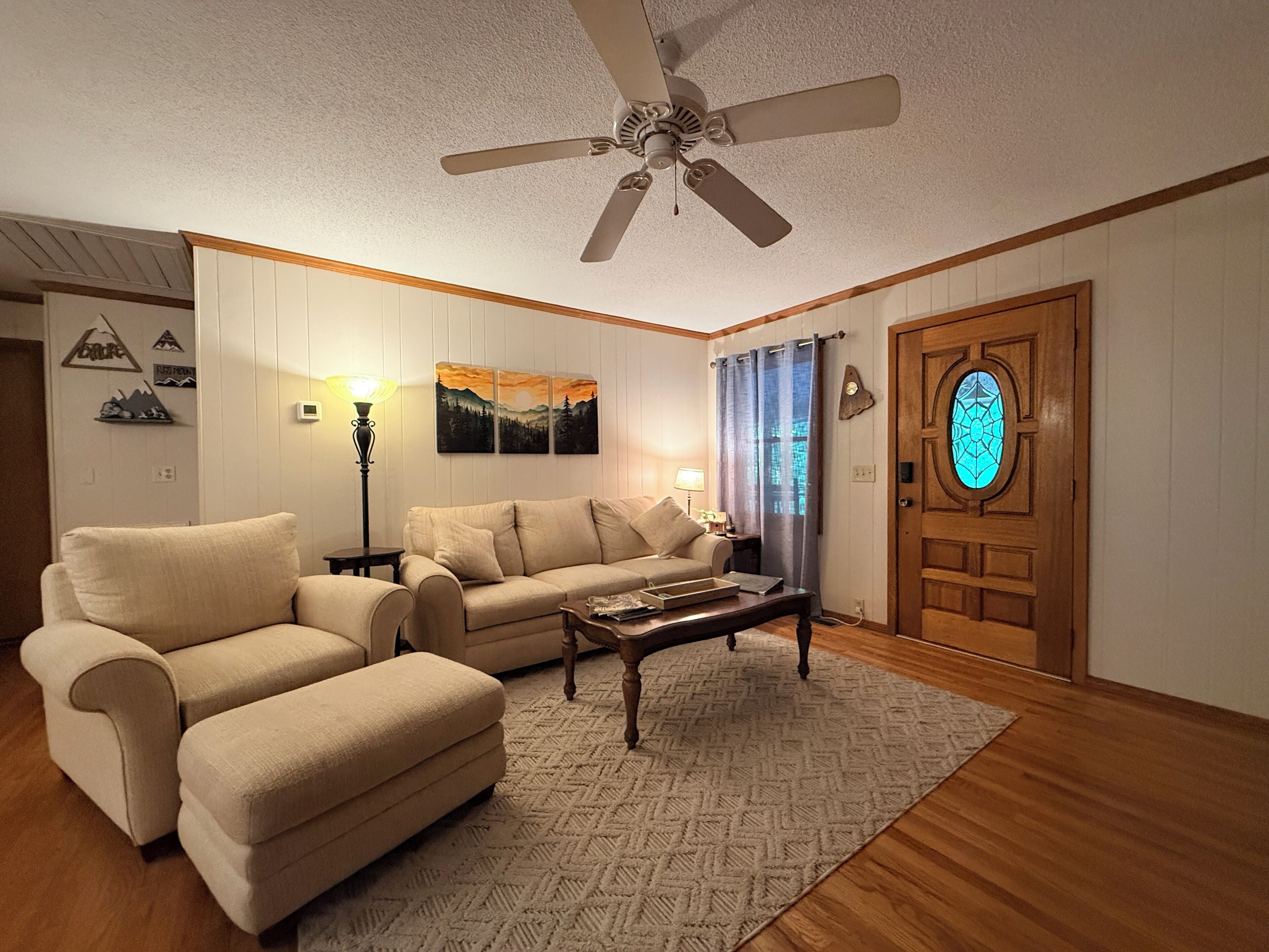 Un salon avec un ventilateur de plafond, un canapé, une table basse et une porte ornée d’un vitrail.