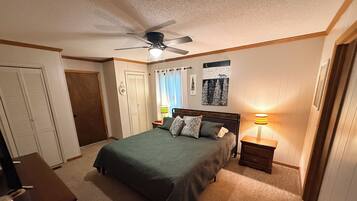 A bedroom with a bed, a nightstand, a ceiling fan, a lamp, and a door.