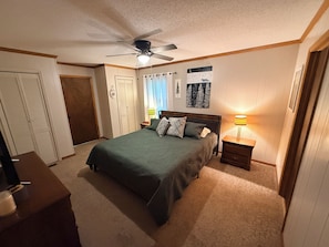 A bedroom with a bed, a nightstand, a ceiling fan, a lamp, and a door. - Howling Hideaway - Woodland Retreat, 2 king beds, Hot tub (Mentone)