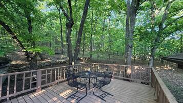 A wooden deck with metal chairs and a table, surrounded by trees.