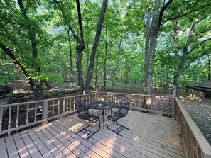A wooden deck with metal chairs and a table, surrounded by trees. - Howling Hideaway - Woodland Retreat, 2 king beds, Hot tub (Mentone)