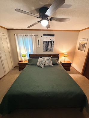 Ein Schlafzimmer mit einem Bett, zwei Nachttischen, einem Deckenventilator und einer Wand mit einem Poster.