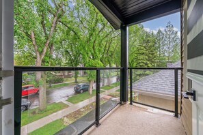 Ein Balkon mit Blick auf eine Wohnstraße, ein rotes Auto ist auf der Straße geparkt, und der Himmel ist wolkenlos.