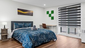 Une chambre moderne avec un lit, un bureau et une fenêtre équipée de stores.