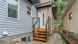 Un immeuble résidentiel avec un escalier en bois menant à la porte d’entrée, un petit porche et un chemin piétonnier en béton.