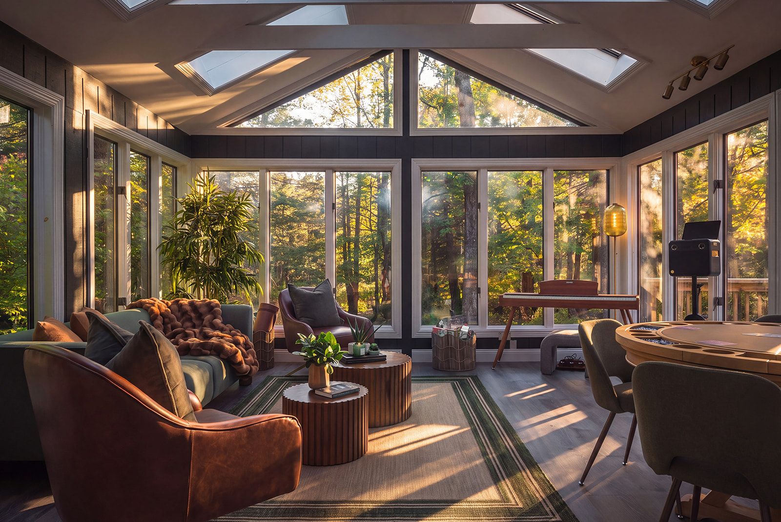 A sunlit room with large windows, a sofa, a chair, a coffee table, and a dining table.
