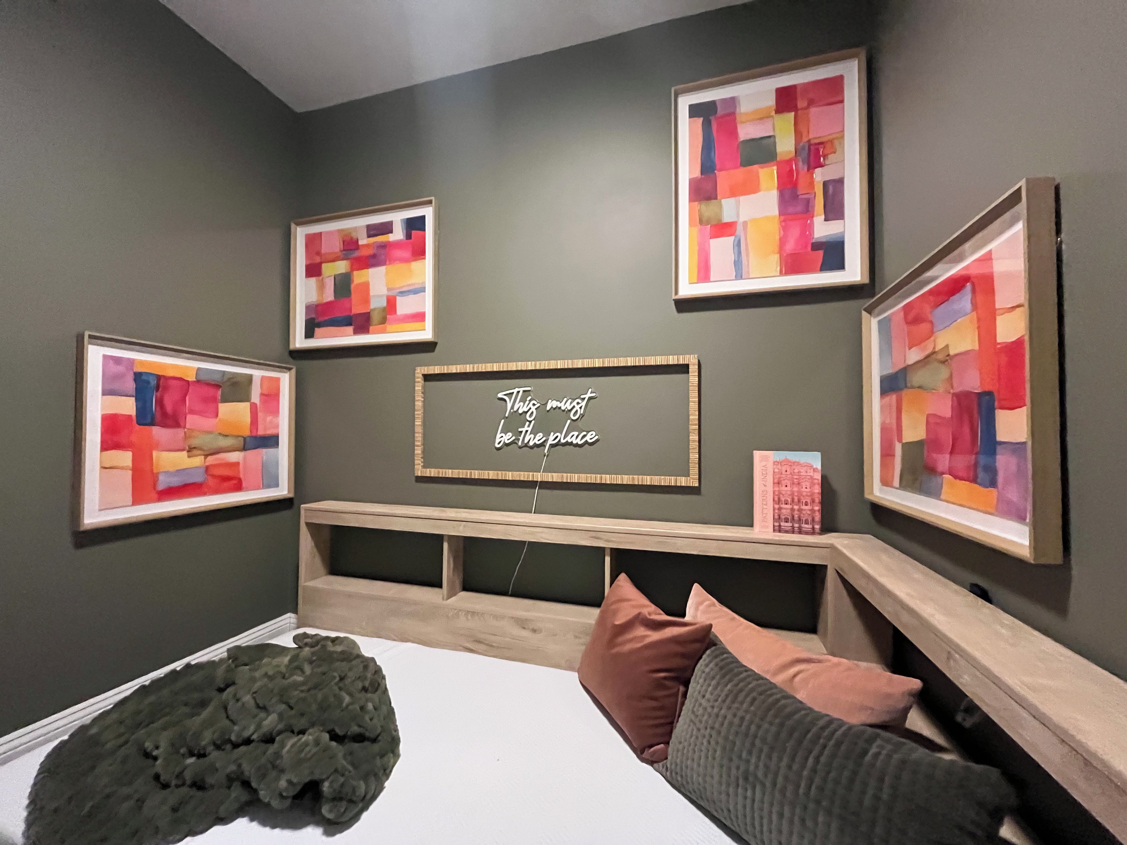 Ein Schlafzimmer mit einem Bett, einem Kopfteil, einem Wandregal und vier gerahmten Kunstwerken.