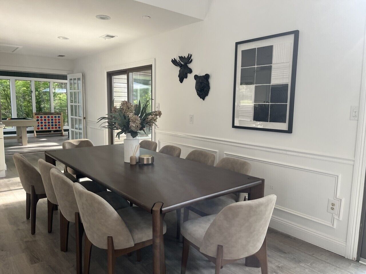 A dining area with a long table and chairs, a vase with flowers, and wall-mounted animal head decorations.