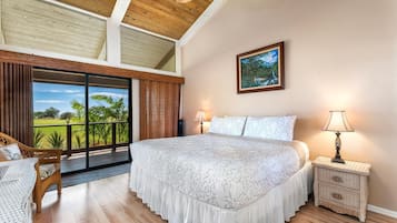 Un dormitorio con una cama grande, una mesita de noche, una lámpara, un cuadro y vistas a un paisaje verde a través de una puerta corredera.