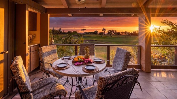 A dining area with a table set for four, overlooking a golf course at sunset. - Waikoloa Villas#a203:top Floor Beauty, Ocean Views (Waikoloa)