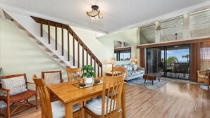 A spacious living area with a wooden dining table, chairs, a sofa, and a staircase. - Waikoloa Villas#a203:top Floor Beauty, Ocean Views (Waikoloa)