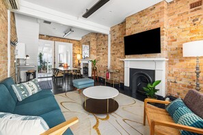 A modern living room with a brick wall, a fireplace, a flat-screen TV, and a dining area.