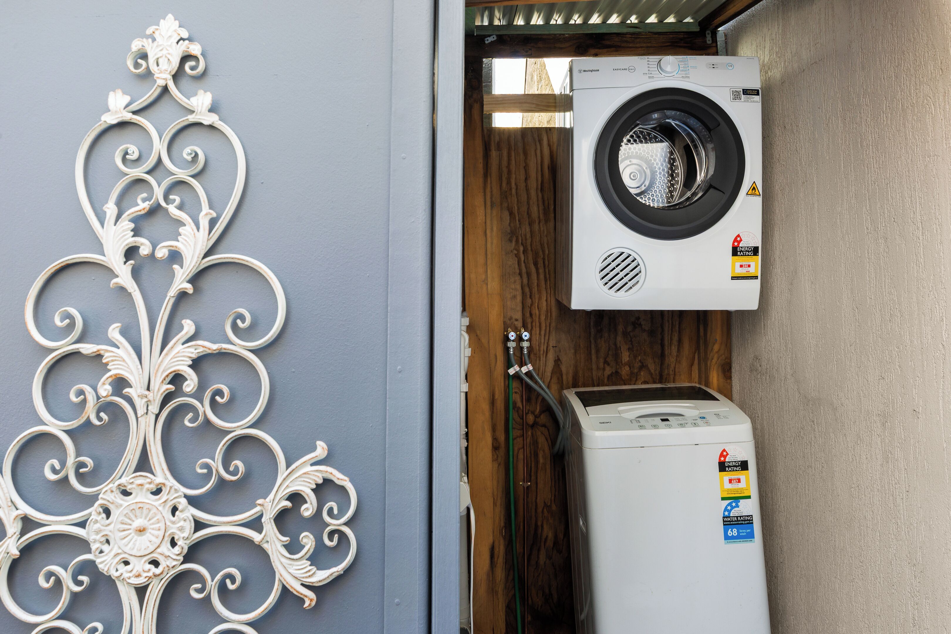 A compact laundry area with a washing machine and dryer, a decorative metal wall piece, and visible plumbing.