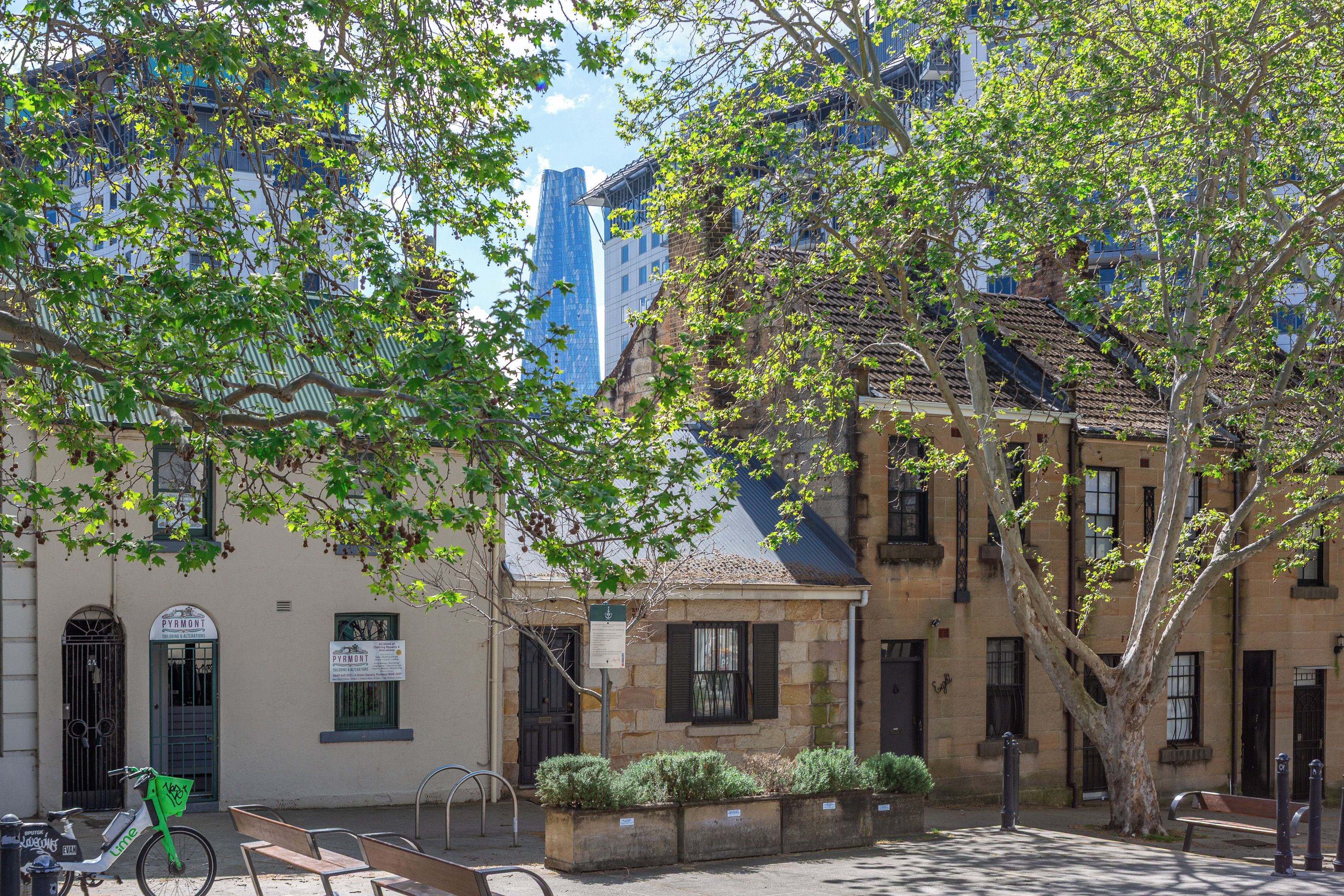 A street scene with a building that has a sign for 'PYRMONT Tailoring & Alterations'. There is a bicycle parked in front of the building.