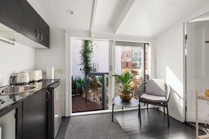A modern kitchen with a built-in oven, a dining area with a chair and table, and a view of the outside through a glass door.
