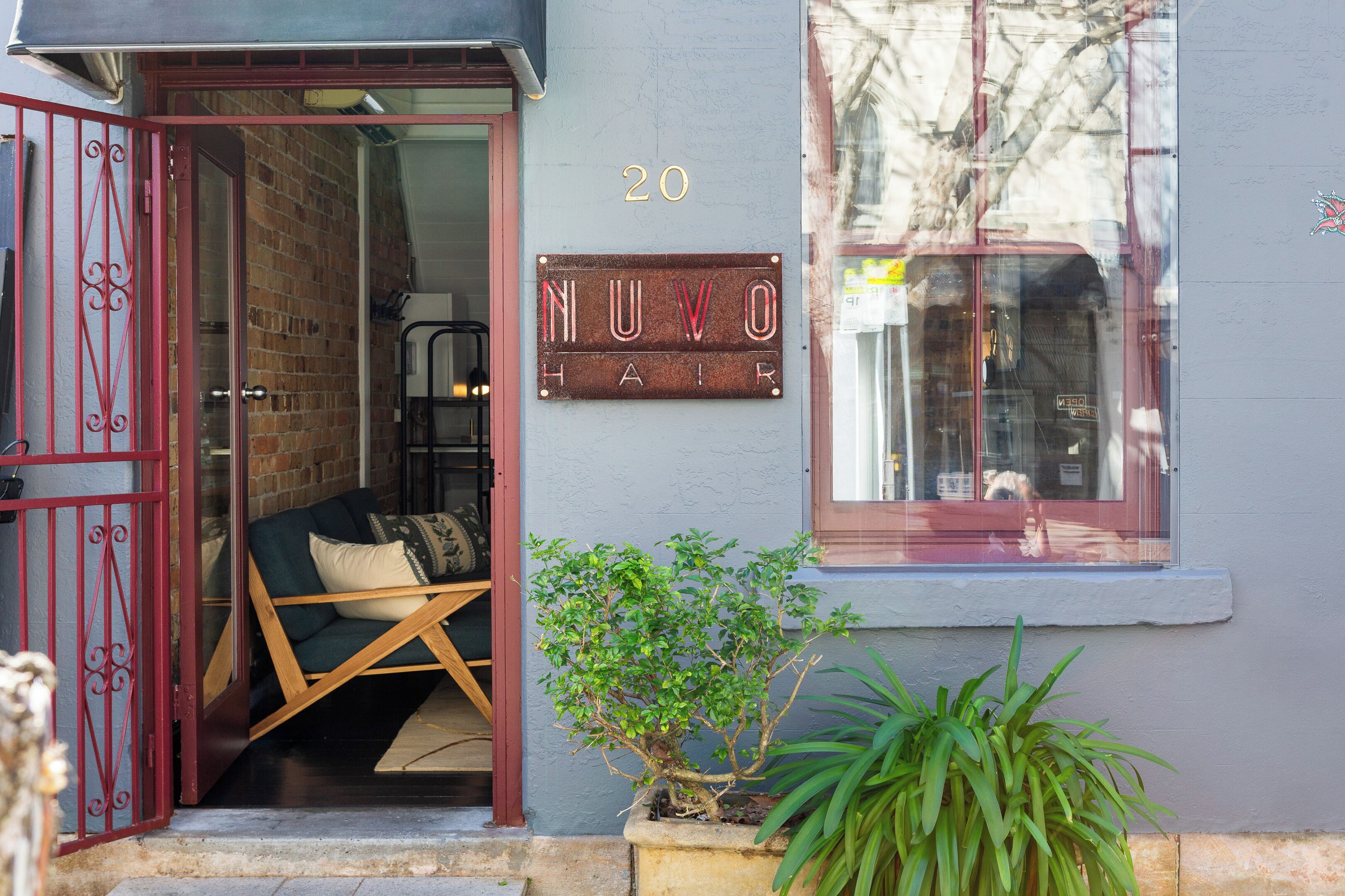 Une entrée d’immeuble avec un portail rouge, une enseigne indiquant « NUVO AIR » et une petite plante en pot.