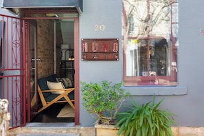 Une entrée d’immeuble avec un portail rouge, une enseigne indiquant « NUVO AIR » et une petite plante en pot.
