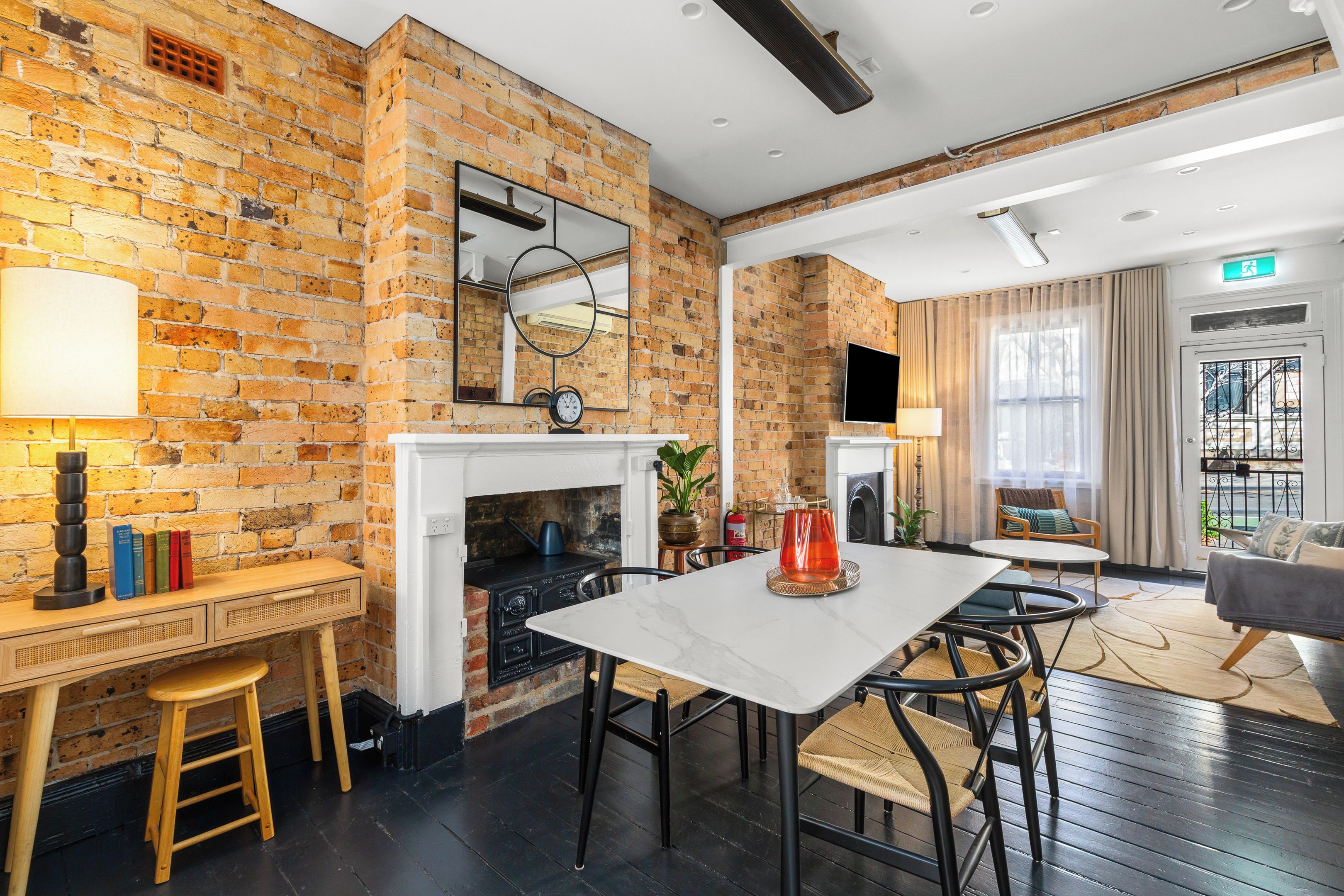 Une chambre d’hôtel moderne avec des murs en briques apparentes, une cheminée, un coin repas avec une table et des chaises, et un espace détente avec un canapé.