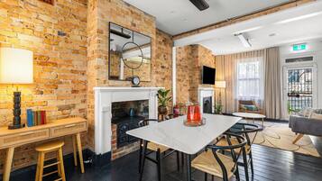 Une chambre d’hôtel moderne avec des murs en briques apparentes, une cheminée, un coin repas avec une table et des chaises, et un espace détente avec un canapé.