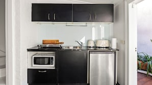 Una cucina compatta con mobili neri, un forno a microonde, un piccolo frigorifero e una macchina da caffè.