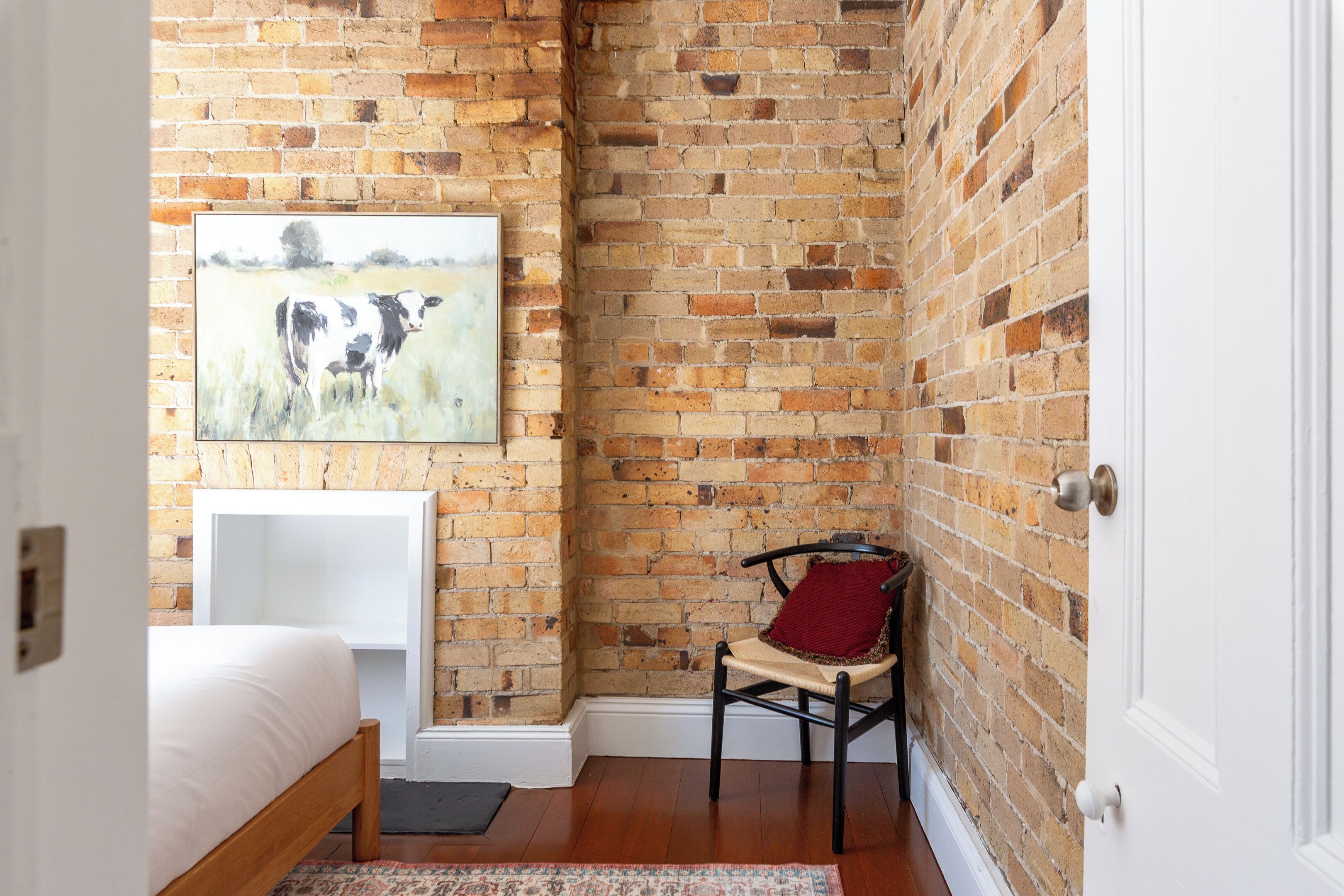 A room with a brick wall, a bed, a chair, and a painting.