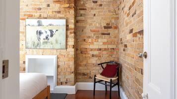 A room with a brick wall, a bed, a chair, and a painting.